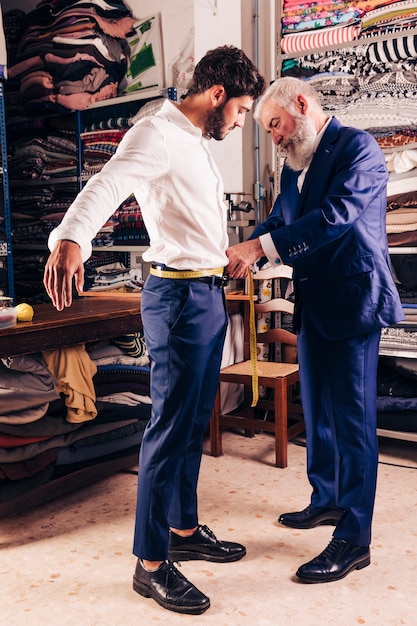 Senior male fashion designer's hand taking measurement of his customer's waist with yellow measuring tape