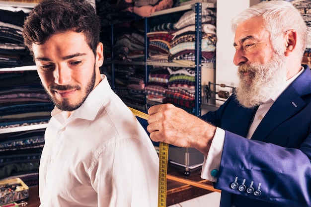 senior male fashion designer taking measurement of his customer in the shop