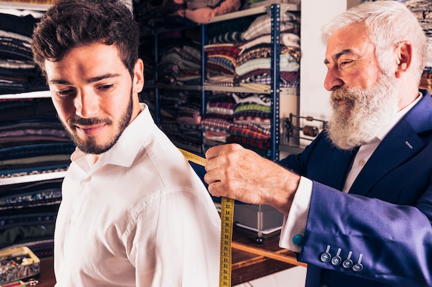 Старший мужской модный дизайнер измерения его клиента в магазине