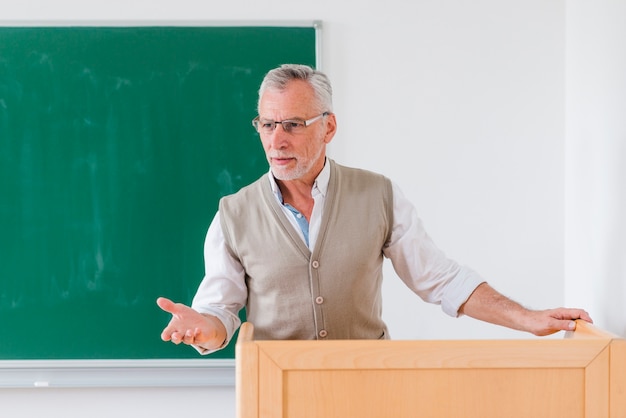 Senior male professor explaining lesson near chalkboard