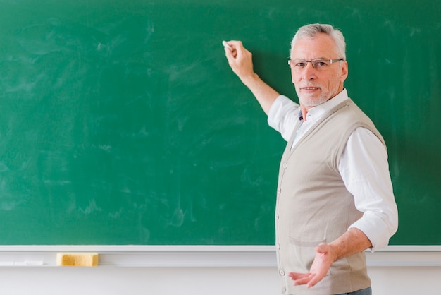 Senior male professor explaining and writing on green chalkboard 