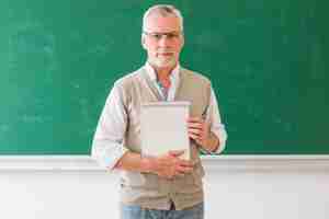 Free photo senior male professor holding notebook standing against blackboard