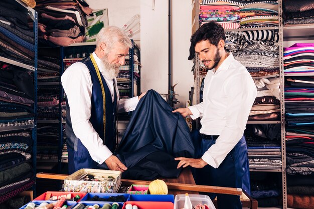 Senior male seller offering fabrics to young man in textile shop