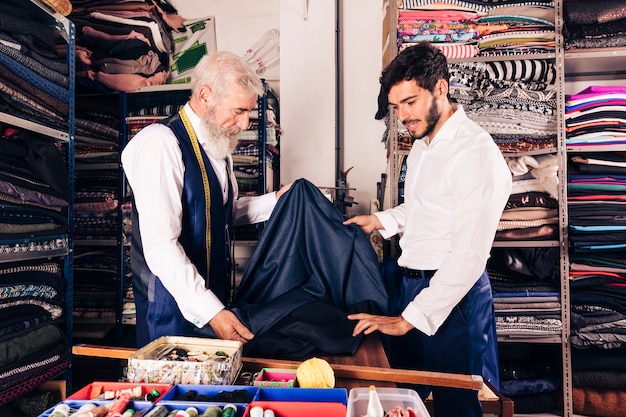 Senior male seller offering fabrics to young man in textile shop