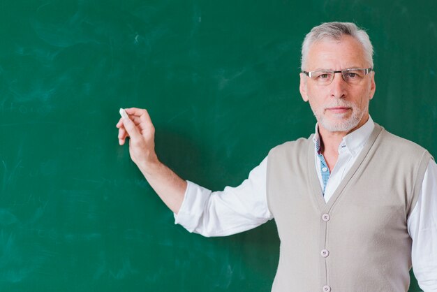 Senior male teacher writing on green chalkboard