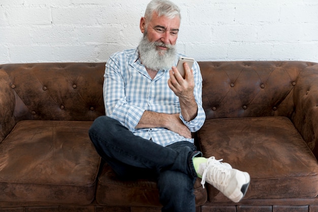 Senior male using smartphone and sitting in sofa