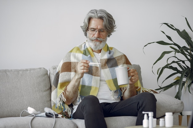 Senior man alone sitting on sofa. Sick man covered with plaid.