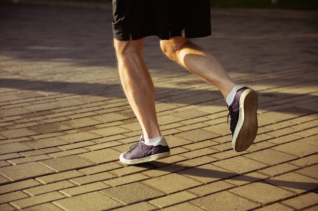 Старший бегун на городской улице. Закройте снимок ног в кроссовках. Кавказская мужская модель бег трусцой и кардио-тренировка в летнее утро. Здоровый образ жизни, спорт, концепция деятельности.