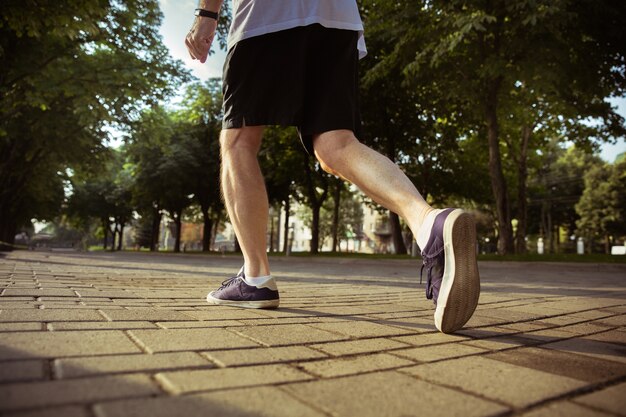 Uomo anziano come corridore in strada della città. immagine ravvicinata di gambe in scarpe da ginnastica. modello maschio caucasico fare jogging e allenamento cardio nella mattina d'estate. stile di vita sano, sport, concetto di attività.