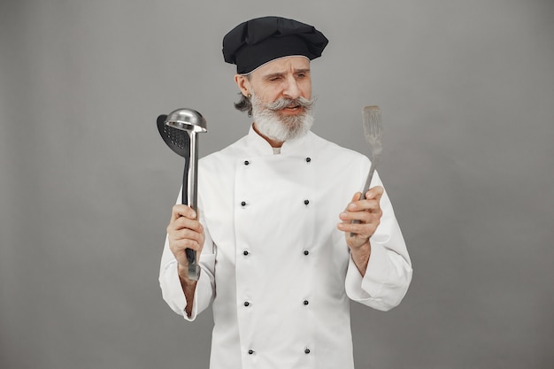 Бесплатное фото Старший мужчина выбирает ковши. повар в черной кепке в голове. профессиональный подход к делу.