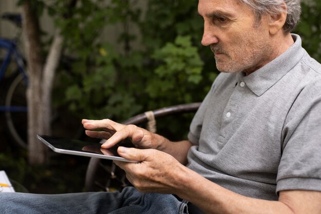 屋外でタブレットでオンラインクラスをやっている年配の男性