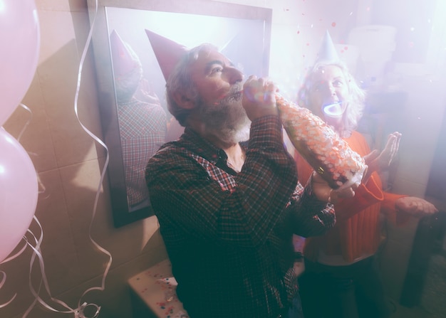Senior man drinking the alcohol through bottle with his wife throwing confetti in the air