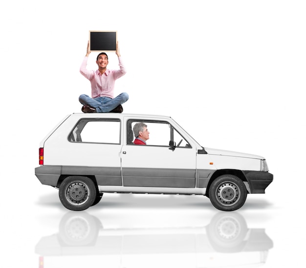 Senior man driving while another man is sitting on the car roof with a blackboard