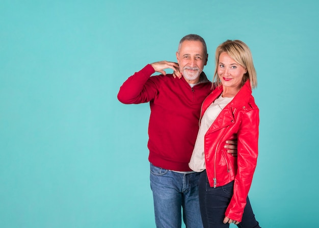 Senior man embracing his girlfriend standing against turquoise background