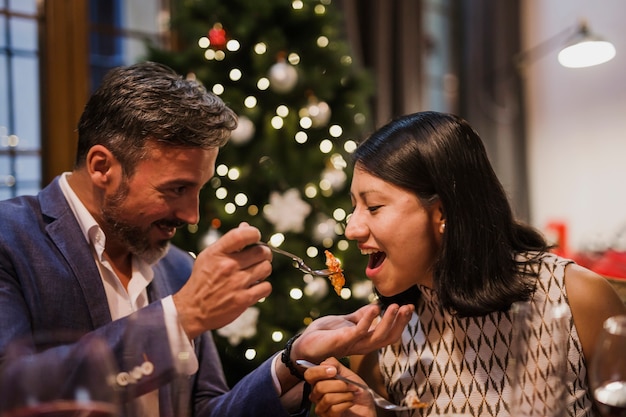 Senior man feading his spouse in front of the christmas tree