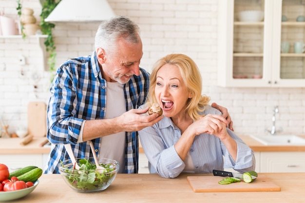 Free photo senior man feeding the mushroom to her wife in the kitchen