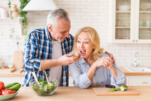 Senior man feeding the mushroom to her wife in the kitchen