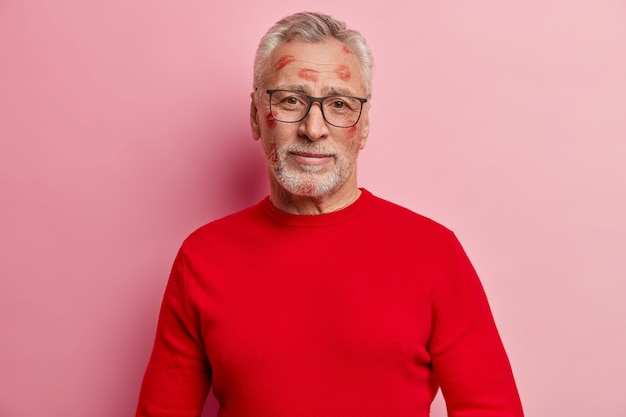 Senior man having lipstick stains on face and wearing red sweater