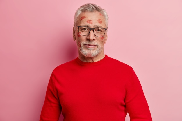 Старший мужчина в красном свитере с пятнами помады на лице
