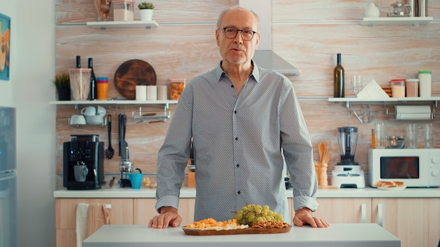 Uomo anziano che fa una videochiamata in cucina mentre la sua famiglia prepara la cena in sottofondo. pov online internet moderno conferenza, chat, comunicazione, conversazione in chat chiamata tramite webcam