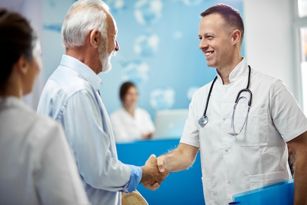 Senior man and his doctor shaking hands while greeting in a hallway at medical clinic Focus is on doctor