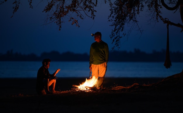 Senior man  and his friend warming his hands with the flames of a bonfire at cold weather in early moring, copy space