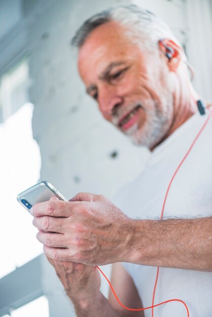 Senior man holding cellphone listening music through earphone