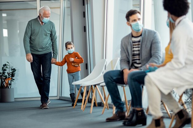コロナウイルスパンデミックの間に診療所に来ている間孫娘と手をつないでいる年配の男性