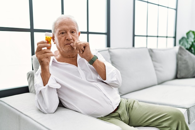 Free photo senior man holding pills mouth and lips shut as zip with fingers. secret and silent, taboo talking