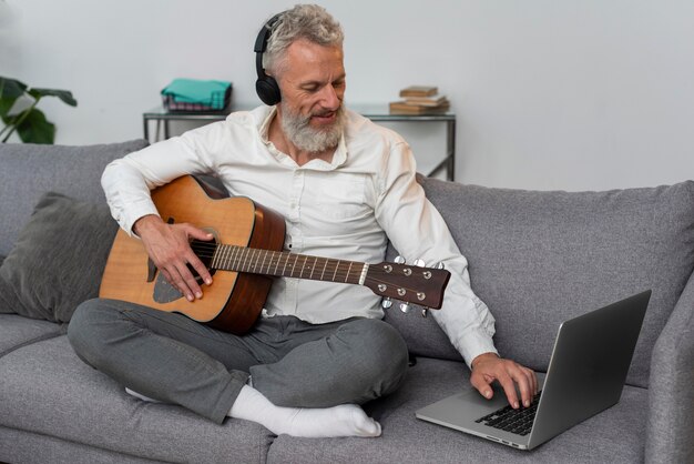 Senior man at home on the couch using laptop to study guitar lessons