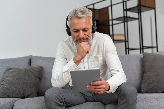 Senior man at home on the couch using tablet device and headphones