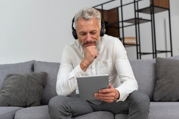 Senior man at home on the couch using tablet device and headphones