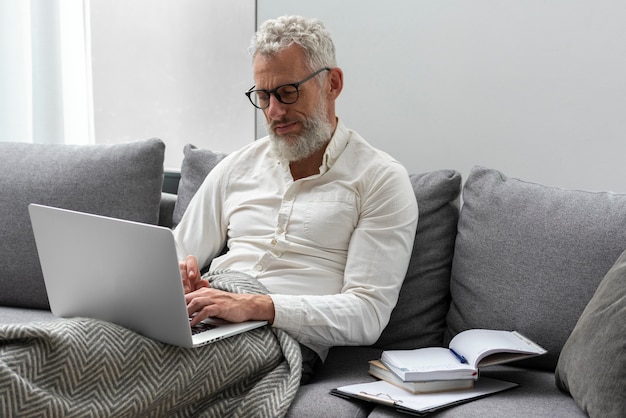 Senior man at home studying on the couch using laptop