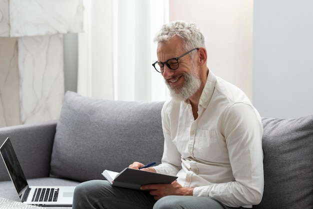 Senior man at home studying on laptop and taking notes