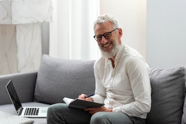 Senior man at home studying on laptop and taking notes