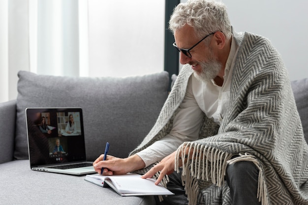 Uomo anziano a casa che studia sul laptop e prende appunti