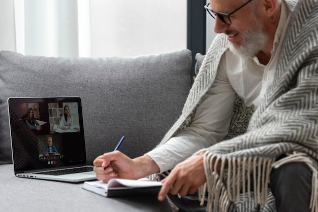 Senior man at home studying on laptop and taking notes