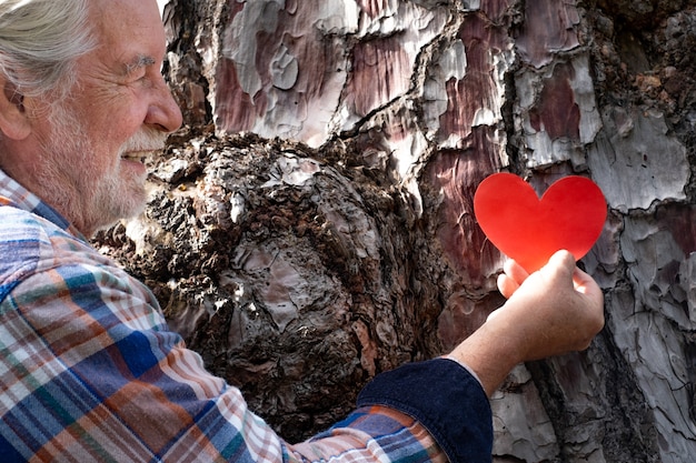 Старший мужчина в лесу кладет форму сердца на ствол дерева. концепция дня земли. вместе спасем планету от вырубки лесов
