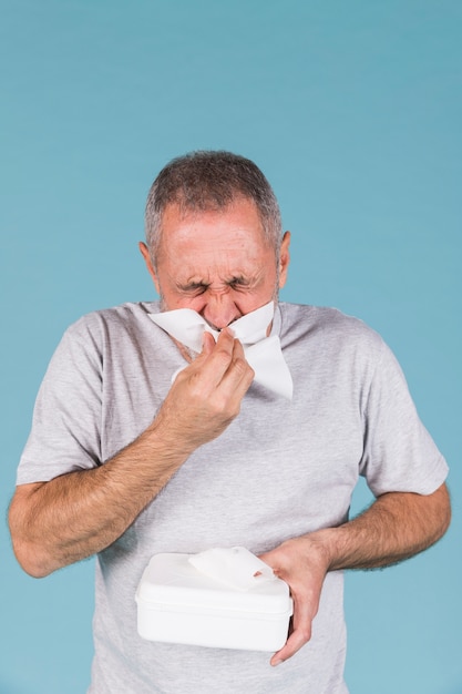 Uomo anziano infettato dal raffreddore e dall'influenza che gli soffia il naso in carta velina