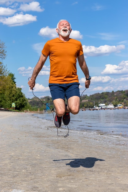 Senior man jumping the rope, exercising on the beach.