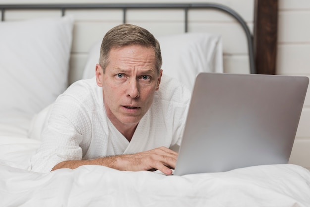 Senior man looking concerned on his laptop in bed