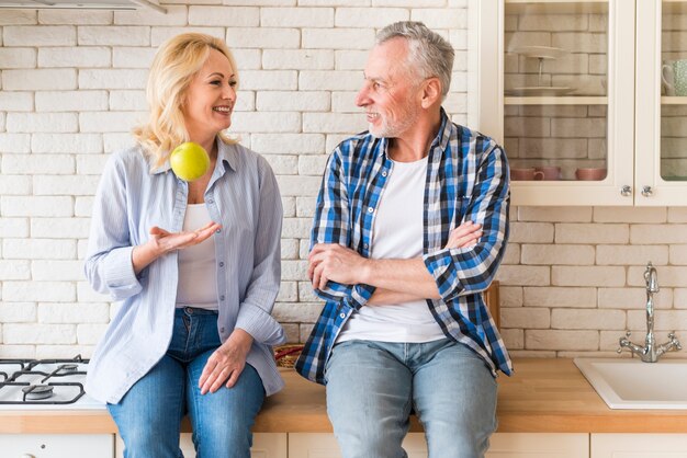 Senior man looking at his wife throwing green apple in the kitchen