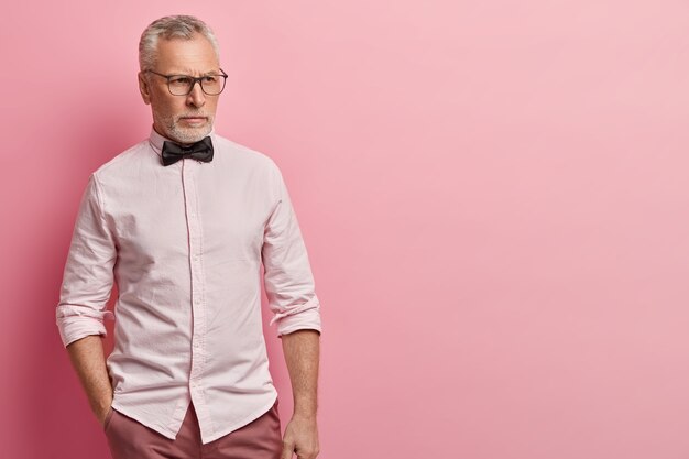 Старший мужчина в розовой рубашке и черном галстуке-бабочке