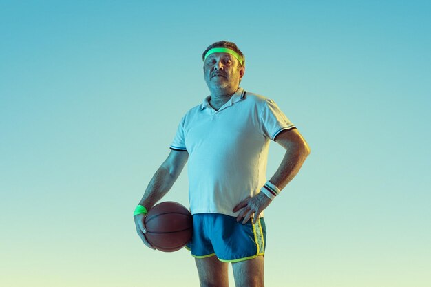 Senior man playing basketball on gradient background in neon light. Caucasian male model in great shape stays active, sportive. 