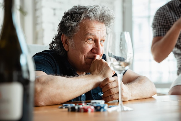 Free photo senior man playing cards and drinking wine with friends