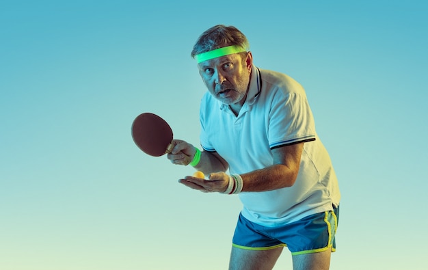 ネオンの光の勾配壁で卓球をしている年配の男性