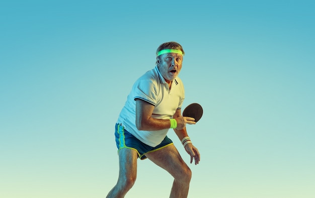Senior man playing table tennis on gradient wall in neon light