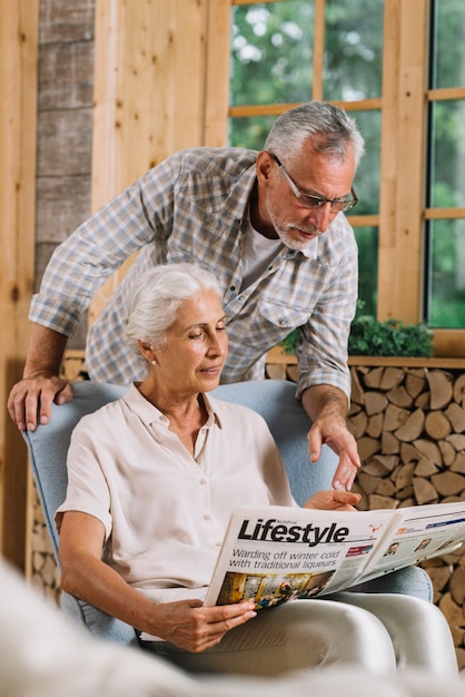 Senior man pointing at newspaper hold by her wife