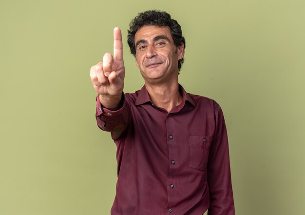 Senior man in purple shirt looking at camera smiling confident showing index finger 