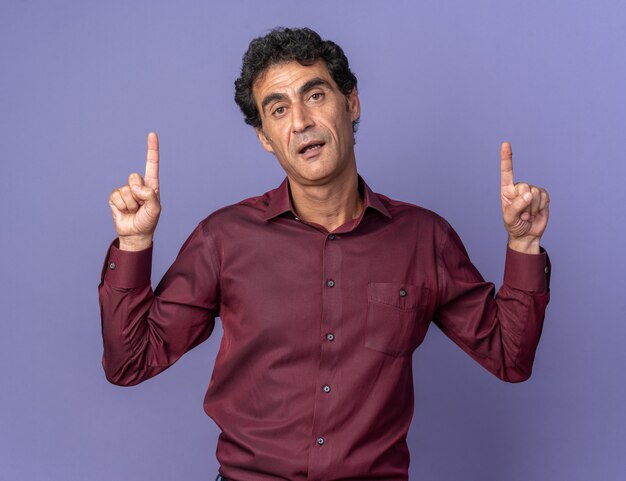 Senior man in purple shirt looking at camera with serious confident expression pointing